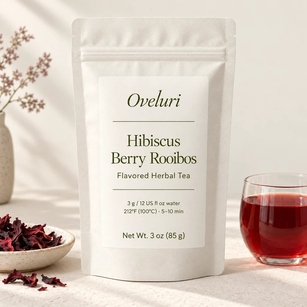 AI packaging concept for Oveluri Hibiscus Berry Rooibos, 3 oz (85 g): white pouch with an olive italic wordmark, beside hibiscus petals and red tea. Final label and delivered packaging pending supplier approval.